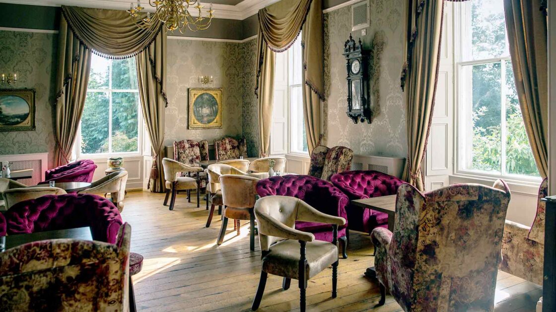 Elegant sitting room with vintage chairs, plush velvet, and large windows offering garden views in a historic hotel.