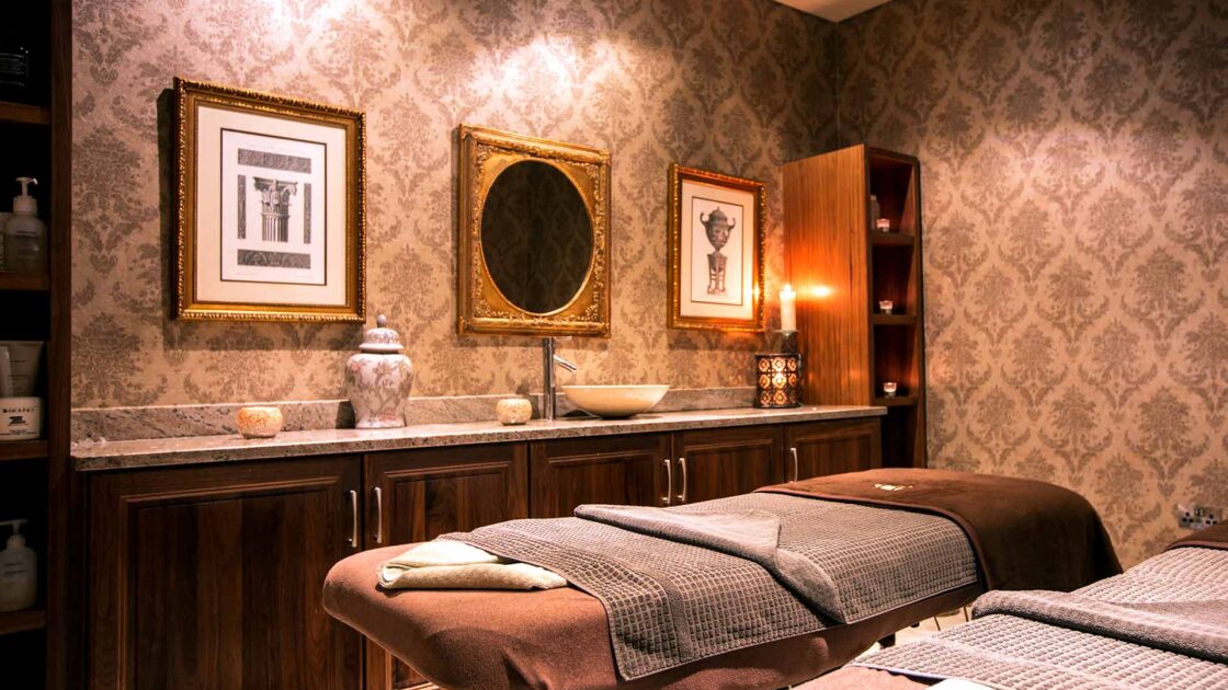 Luxurious spa room with plush massage tables, elegant wallpaper, warm lighting, and serene atmosphere for ultimate relaxation.