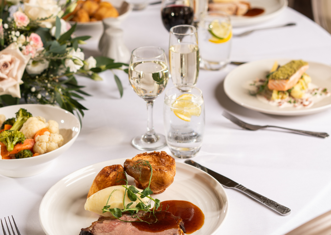 Elegant dining table with roast beef, Yorkshire pudding, wine, and floral centrepiece at luxury hotel restaurant.