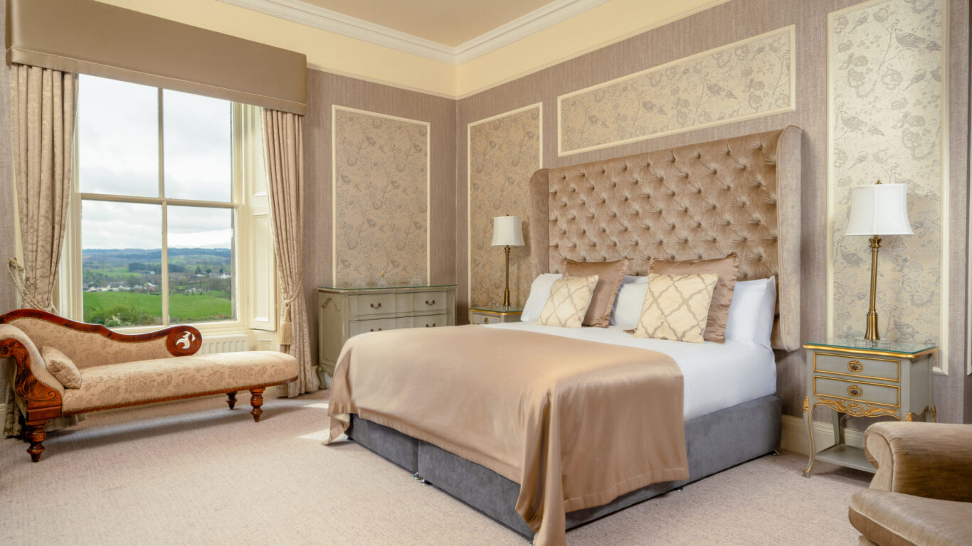 Elegant guestroom with countryside views, plush bed, antique chaise longue, and exquisite decor. Perfect for a serene stay.