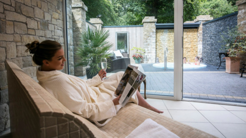 Relaxing in spa lounge with magazine and champagne, overlooking outdoor hot tub and garden view at luxury hotel.