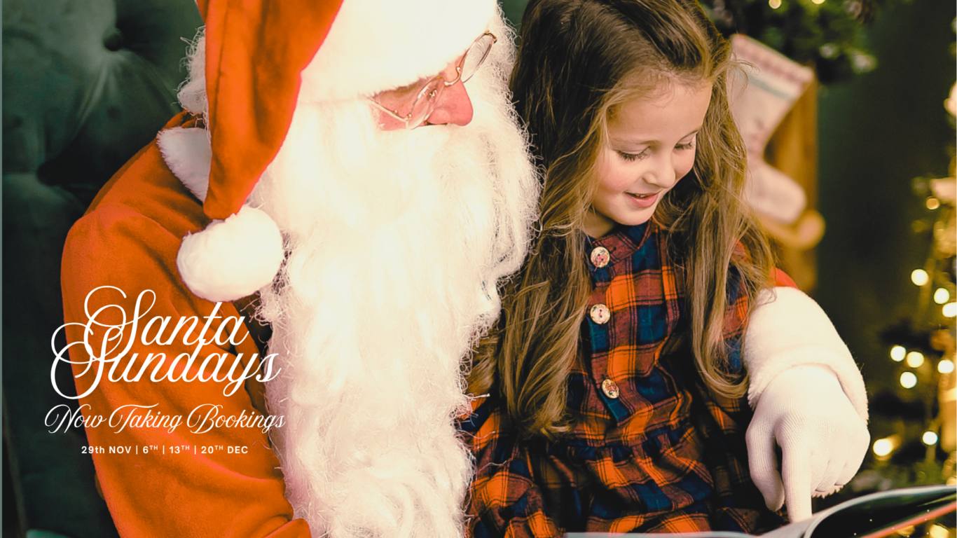 Santa reading a book with a smiling girl in cosy hotel lounge, surrounded by festive decorations, inviting holiday fun.