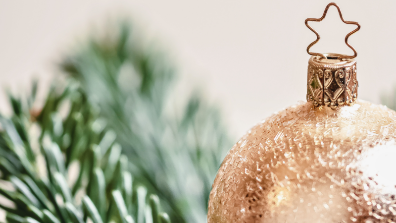 Festive gold ornament with star hook and green pine, evoking holiday warmth at a luxurious hotel stay.