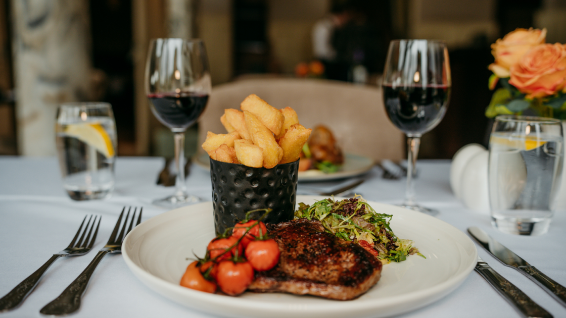Elegant dining with gourmet steak, chips, and wine on a white tablecloth, perfect for a refined hotel restaurant experience.