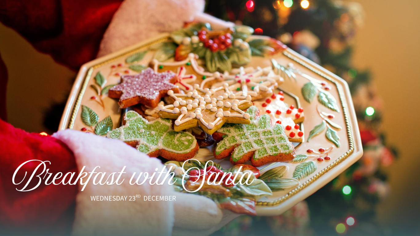 Festive biscuits on decorative plate held by Santa, with Christmas tree in background at the hotel’s Breakfast with Santa.