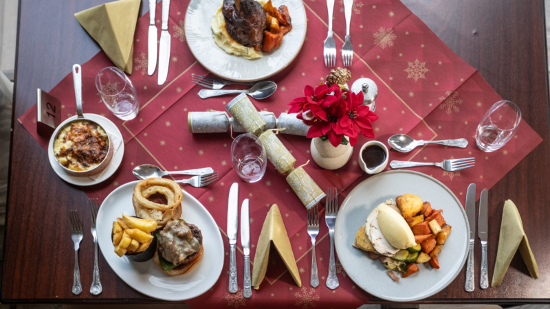 Festive hotel dining table with gourmet dishes, elegant red and gold decor, inviting Christmas ambiance.
