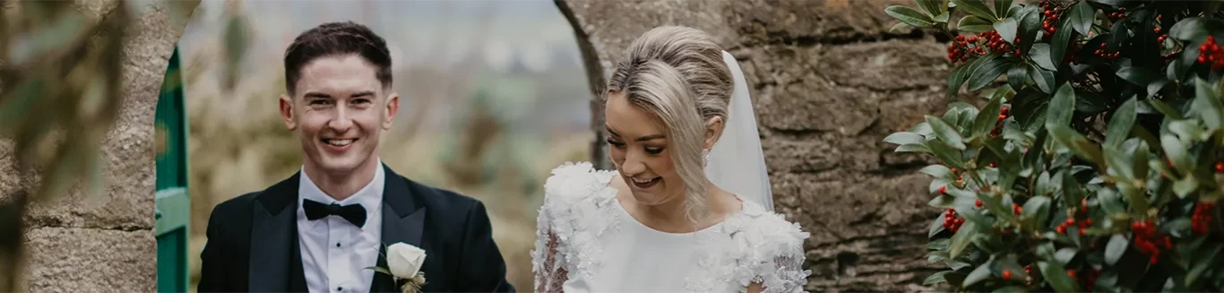 Bride and groom smiling at rustic stone arch, lush greenery, perfect for romantic, countryside weddings.