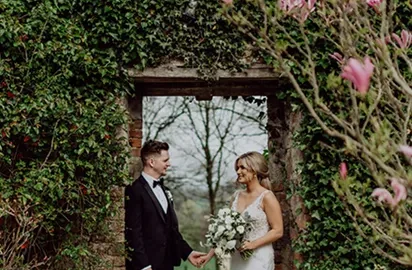 Romantic garden wedding couple under ivy archway, surrounded by blooming magnolias at scenic hotel venue.