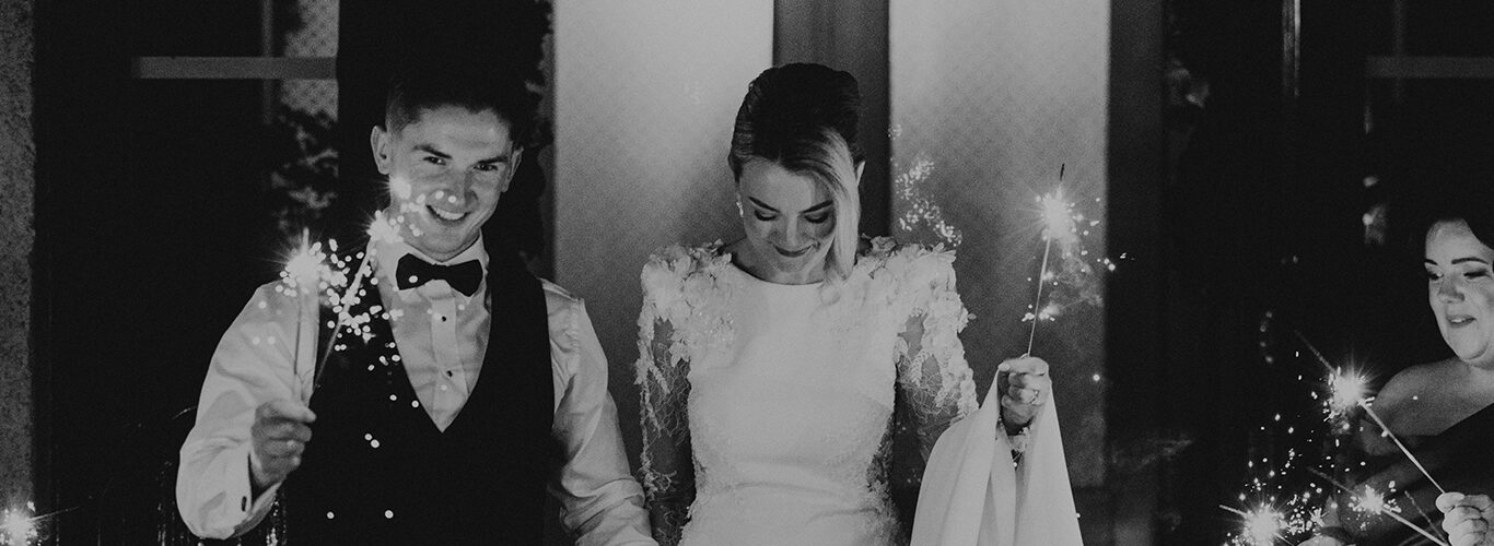 Newlyweds celebrate with sparklers outside elegant hotel entrance, creating a magical evening atmosphere for guests.